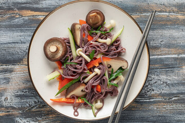 Black rice noodles with shiitake shimeji mushrooms and vegetables on a plate on the table.