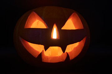 Pumpkin with a carved face and a candle in the dark. Halloween holiday concept