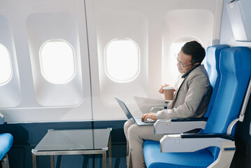 Young Asian executive excels in first class, multitasking with digital tablet, laptop and...