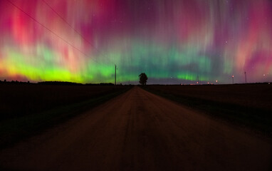 Green, yellow, and red aurora over a rural country road