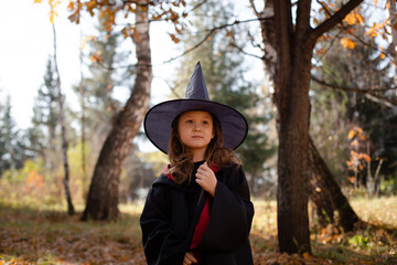 Seven years old girl in black dress, pointed hat and magic wand.