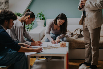 Obraz premium High school students work diligently on a group project with their professor in a cozy home environment. The setting is relaxed, fostering collaboration and focused learning.