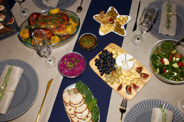 High angle shot of cheese and fruit platter on wooden board and roasted chicken served on festive table setting on Christmas Eve, camera flash, copy space