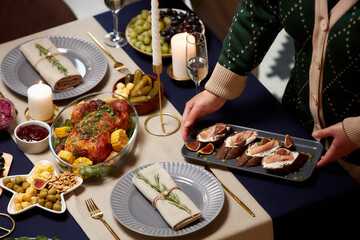 High angle shot of unrecognizable woman serving plate with meat tartine on festive dinner table with roasted turkey on Christmas Eve, copy space