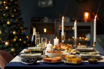 Still life shot of dining table with festive dishes served with champagne glasses and lit candles while Christmas lights are glowing in background, copy space