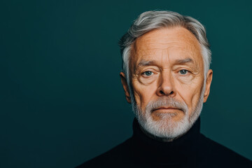 Fototapeta premium Portrait of mature man with grey beard and hair on teal background, calm and reflective expression
