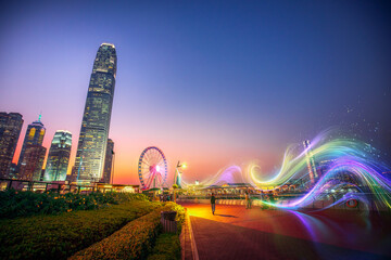 A long exposure photograph of a city skyline at night with a Ferris wheel and light trails.