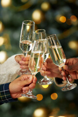 Vertical shot of people clinking glasses with champagne celebrating Christmas together at home...