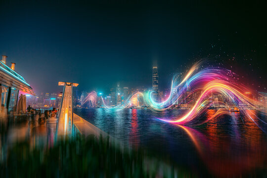 A vibrant cityscape at night with a colorful light trail streaking across the water.
