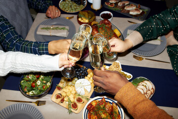 Cropped shot of people raising toast clinking glasses with champagne while celebrating Christmas...