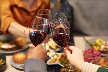 Cropped shot of people clinking wine glasses sitting at festive dining table during friends gathering at home while celebrating Christmas, copy space