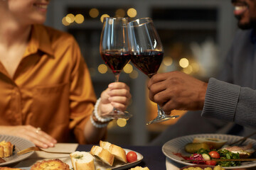 Cropped shot of multiethnic couple enjoying red wine clinking glasses during romantic date at home dinner, copy space