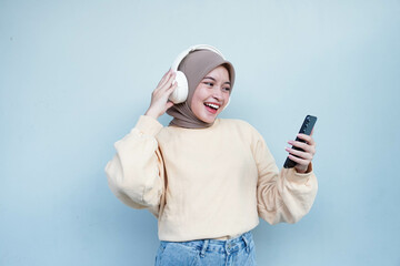 Young Asian muslim woman in cream sweater and wearing headphones for listening to music via mobile...
