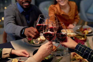 Cropped shot of people clinking wine glasses celebrating Christmas together while sitting at dining table having fun during friends gathering at home party, copy space