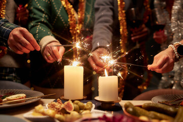 Cropped shot of multiethnic friends lighting bright sparklers from the candle flame while celebrating Christmas together at home party, copy space
