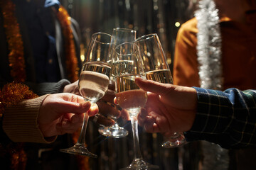 Cropped shot of friends clinking glasses of champagne standing in top light while celebrating...