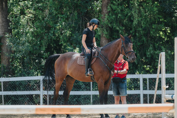 A young rider getting horse riding lessons from an instructor in an outdoor equestrian arena.