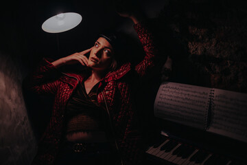 A woman in a red jacket sits thoughtfully beside a piano and sheet music. The dim lighting creates...