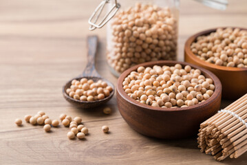 Fototapeta premium Soy bean seeds in wooden bowl, glass jar and spoon on wooden background