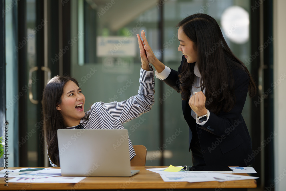 Wall mural Two Asian woman colleagues give each other a high five, Successful business team working together concept.