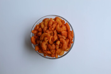Spicy fried small macaroni crackers, inside glass bowl, on white background, flat lay or top view