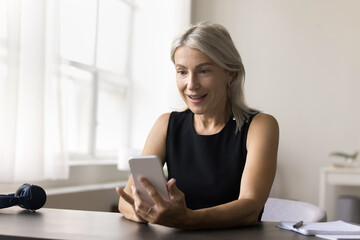 Amazed older age woman work study from home sit at desk look on phone screen receive perfect commercial proposition win online course for free. Excited old female get super present from famous blogger