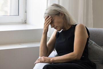 Tired depressed older woman pensioner hold hand on forehead feel headache weakness anxiety...