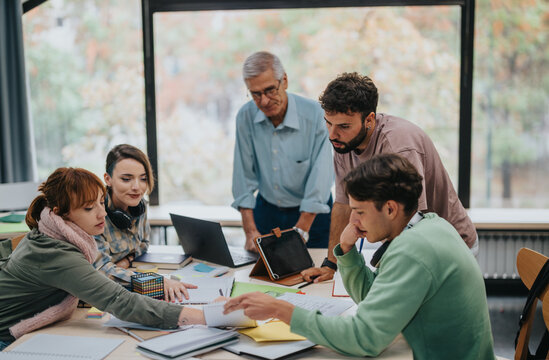 A group of university students working together on a project with their senior professor providing guidance and support. Collaborative learning and teamwork in an educational setting.