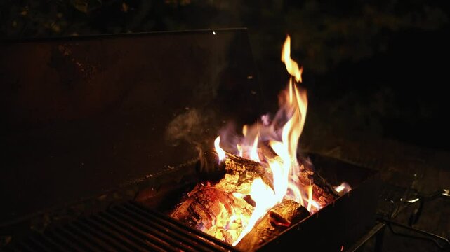 Wood is burning in the barbecue pit at night. A hand is lighting the fire at night. Preparing for a barbecue.