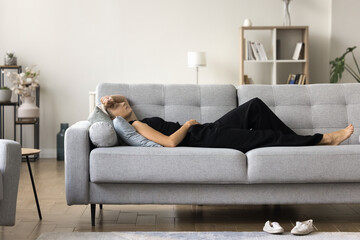 Tired elderly lady rest at home after long difficult work day lie on soft couch in relaxed pose sleep nap daydream. Exhausted aged female lying on sofa at living room feel headache migraine need quiet