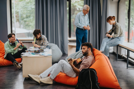 Group of college students engaged in a music class, playing instruments and collaborating in a creative, relaxed environment with bean bags and natural light.