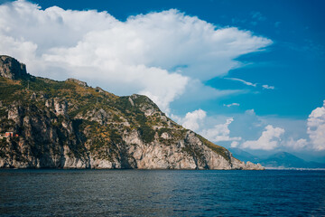 Panoramic view of Amalfi Coast from the sea with clear blue sky, mountains, and coastal buildings. Sunny summer day showcasing scenic landscape, cliffs, and tranquil Mediterranean waters..