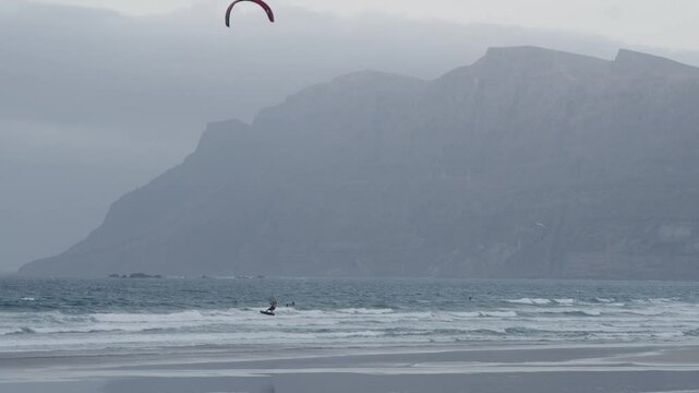 Kite surfer glides across waves at beach near the mountains in Famara, Lanzarote
