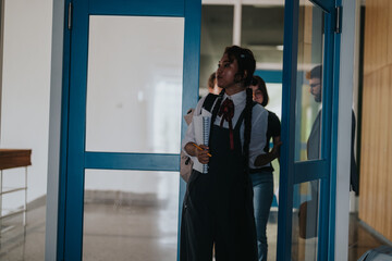 Students holding notebooks walk through a school hallway, discussing coursework and exchanging...