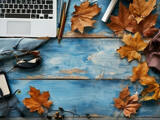 Autumn leaves scattered around a laptop on a wooden table, viewed from above, showcasing a seasonal workspace.