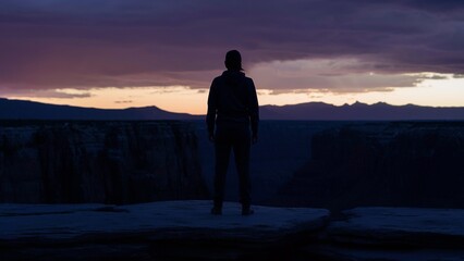 Obraz premium Person in silhouette gazing at twilight canyon from rocky ledge