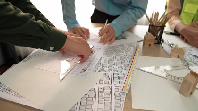Smart architect and safety engineer discussion about building blueprint on table with architectural document, measurement tools and wooden block scatter around at modern office. Closeup. Delineation.