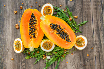 Slices of sweet papaya, passion fruit and rucola surrounded by granola flakes on a wooden background
