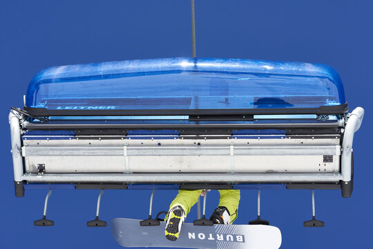 Leitner Chairlift with Burton snowboarder from below. Ropeway transports winter sports athlete Lift in front of blue sky. Up view. Feldberg, Germany.