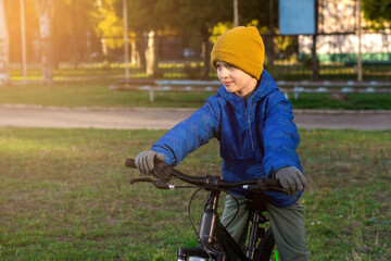 Young child cycling on an autumn day, dressed warmly, with sunset glow and urban landscape behind.