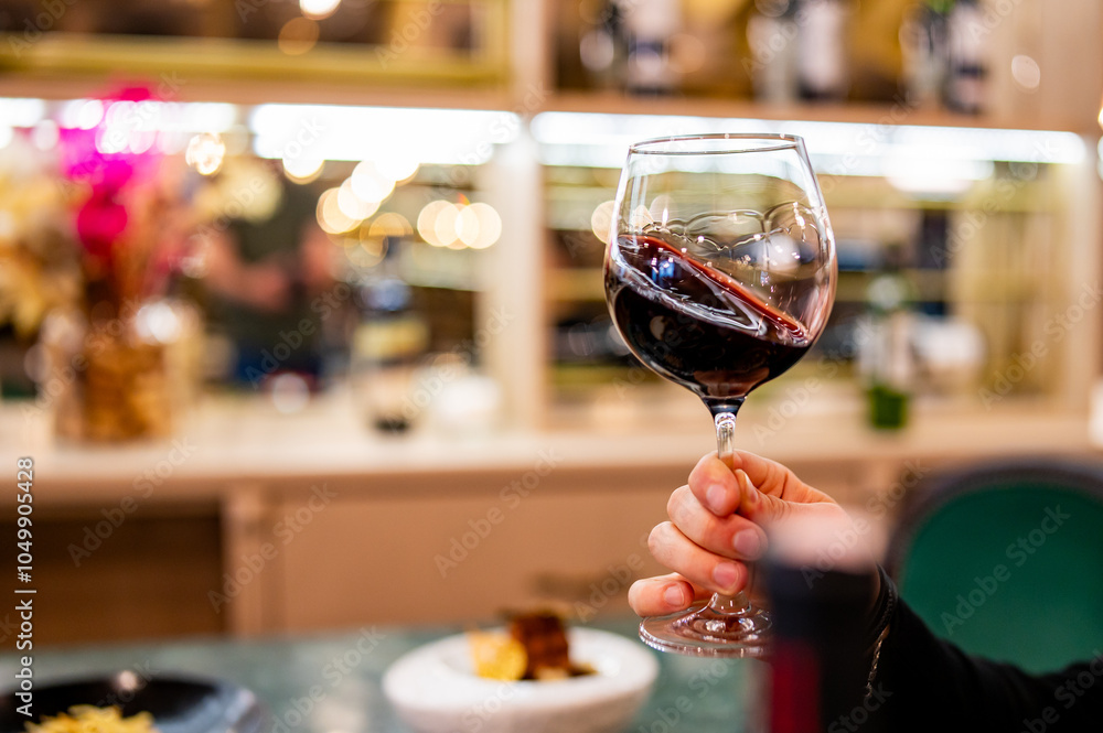 Wall mural a close-up of a hand holding a glass of red wine in a cozy bar or restaurant setting with warm light