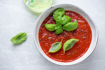 Bowl of tomato soup served with fresh green basil, horizontal shot on a grey granite background, elevated view