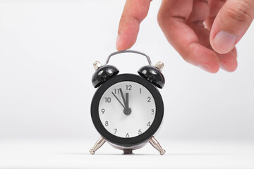 Hand reaching to adjust a classic black alarm clock, symbolizing time management and the importance of punctuality.