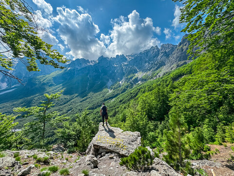 Hiker father with baby carrier backpack on edge of rock formation with panoramic view of Valbona Valley National park surrounded by majestic steep mountain ridges of Albanian Alps, Albania. Wanderlust