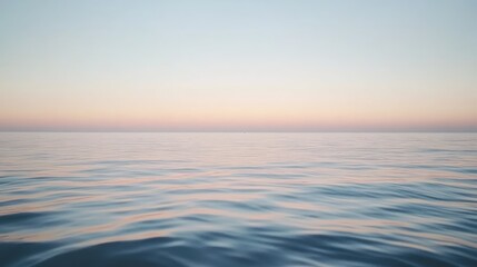 Obraz premium A calm ocean scene at dawn, with the sky and water merging in subtle hues of soft peach, pale blue, and creamy white