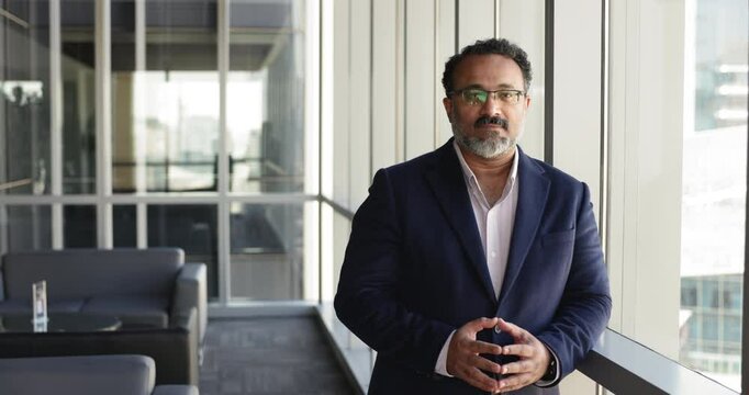 Happy middle-aged businessman in formal jacket stand in modern skyscraper office smile look at camera feels satisfied after successful negotiations. Business trainer, coach or company founder portrait