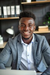 Obraz premium Man in a suit is smiling and sitting at a desk with a laptop. Concept of professionalism and confidence