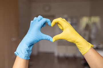 Two hands of a doctor in blue and yellow medical gloves are folded in the shape of a heart, the...