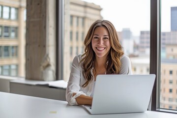 A cheerful young woman sitting at a desk with a laptop in a bright, modern office environment, symbolizing productivity, happiness, and professionalism.