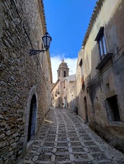 Strolling in streets of Erice city. Medieval town in Sicily. Ancient architecture. Houses and path made of stone. Sunny weather. Blue sky in Italy. Historic towers, churches and castle. Sicilian life.